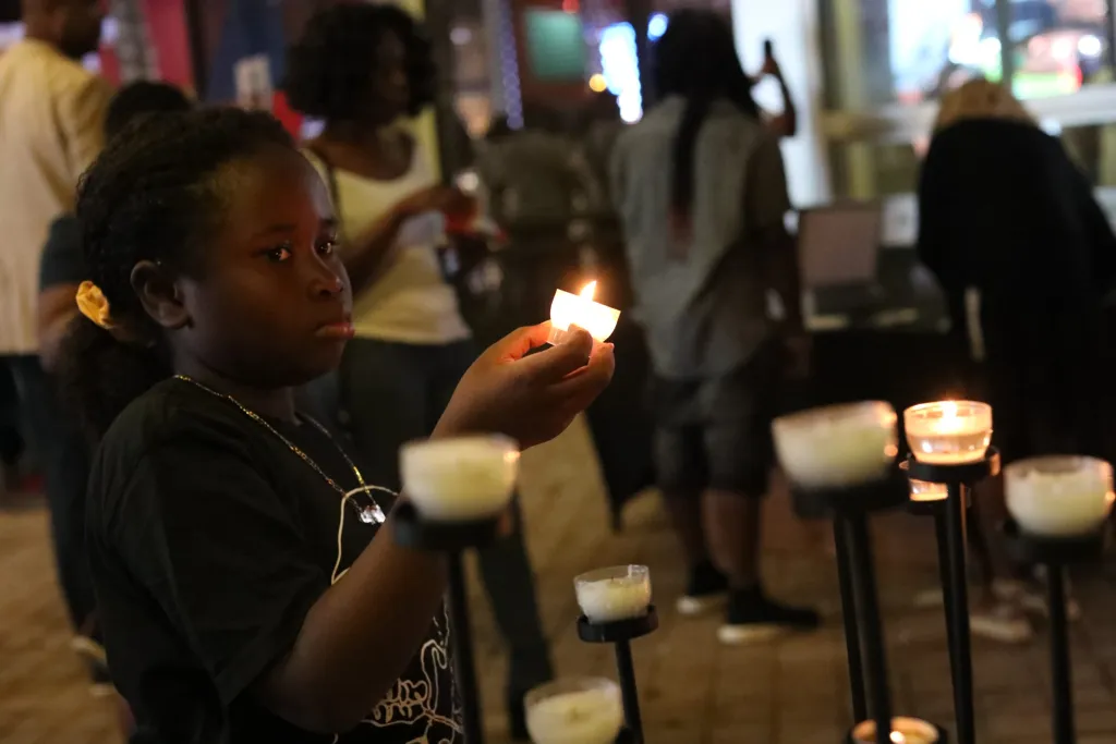 Candles / In front of the Little Haiti Memorial Living Wall, a small girl ignites candles for Mikaben. Photo by Ashley Miznazi for The Haitian Times. October 2022.